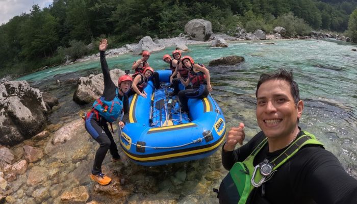 A smiling Bovec Rafting Team guide taking a selfie with happy tourists in a raft on the Soča River.