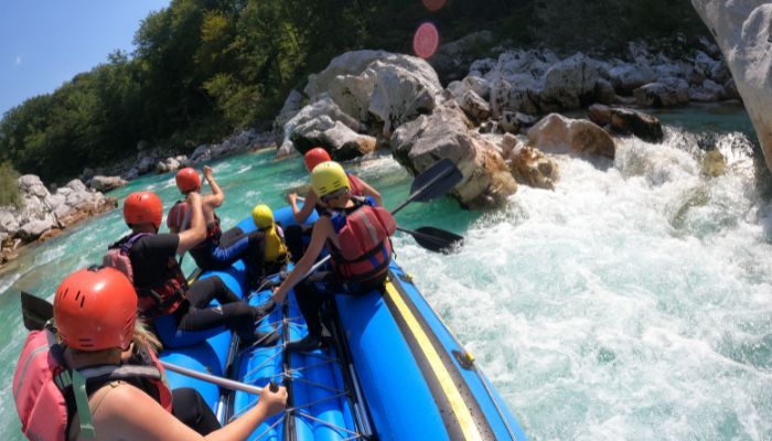 family-rafting-teamwork-soca-bovec Family rafting on the Soča river in Bovec with adults paddling and kids sitting safely in the middle of the raft.