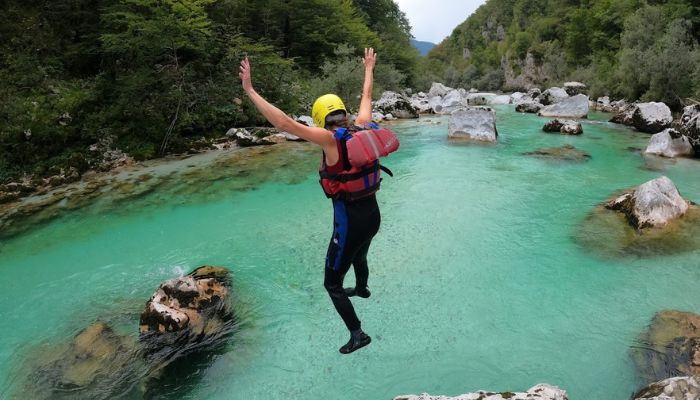A teenager jumping into the emerald Soča River from a rock during a family rafting trip in Bovec, Slovenia.