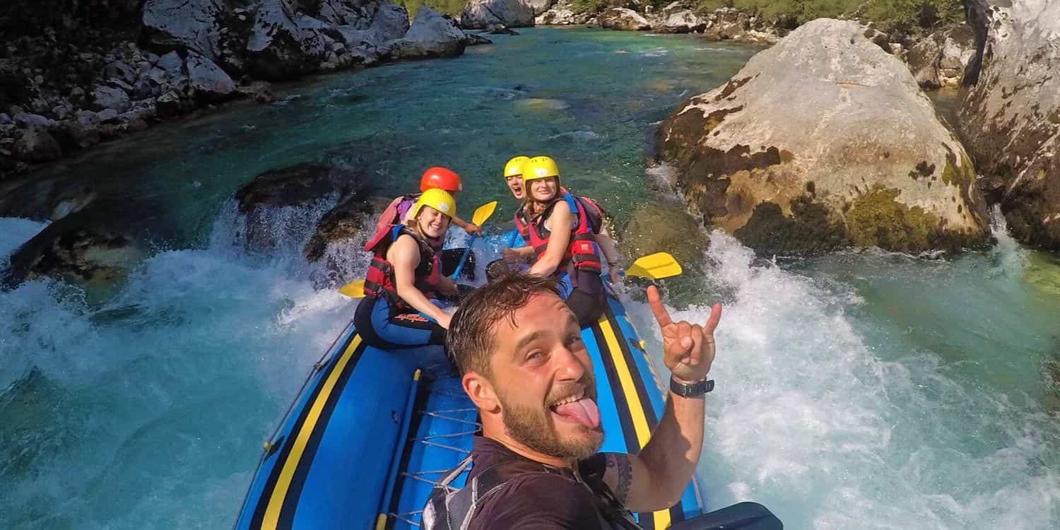 Licensed rafting guide taking a selfie with a group of happy beginners in a raft on the emerald Soča River in Bovec, Slovenia.