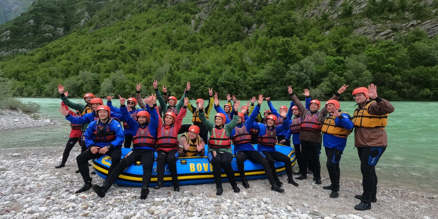 Happy group in neoprene suits and helmets raising hands by Soča River