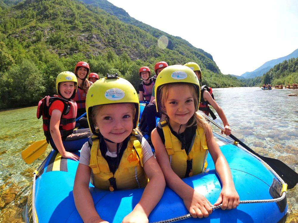 Two young girls laughing on a rafting boat during a family-friendly tour on Soca River in Bovec, Slovenia.