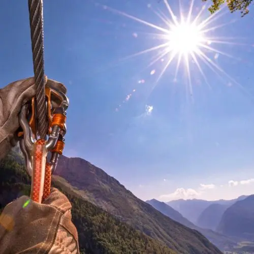 Close-up of professional zipline pulley and carabiner on a steel cable with bright sun in the background at Kanin Park.