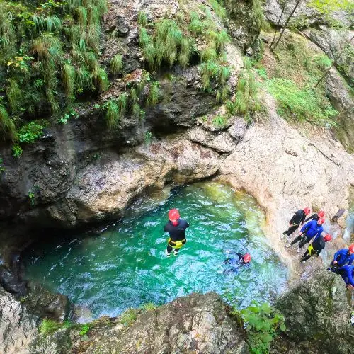 An adventurous guest jumping from a crystal-clear waterfall into a deep emerald pool in Sušec Canyon.