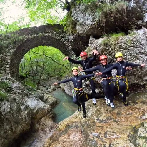 A happy family posing in front of the historic stone bridge at the entrance of Sušec Canyon, Bovec.