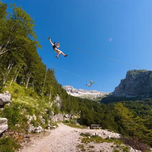 A person gliding on a zipline wire with a spectacular panoramic backdrop of the Julian Alps peaks.
