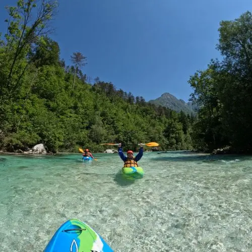 A happy kayaker raising their paddle in triumph while navigating a moderately challenging rapid on the Soča river.