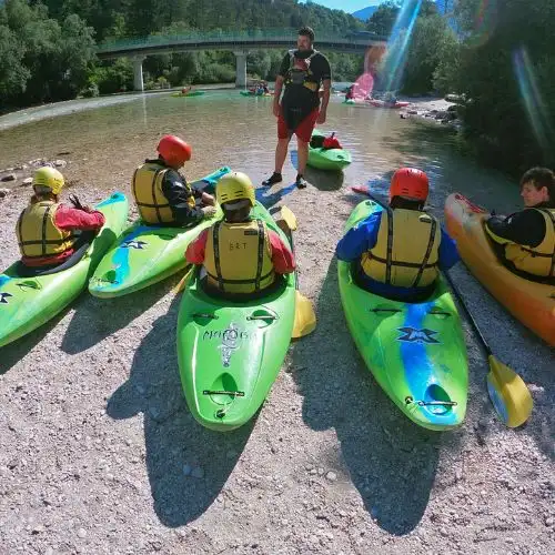 Professional kayak instructor giving a safety briefing to guests sitting in their kayaks on the banks of the Soča river.