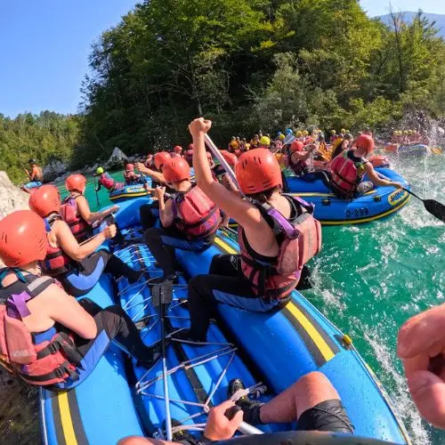 Multiple rafting boats with groups of friends having a water fight on a calm section of the Soča River.