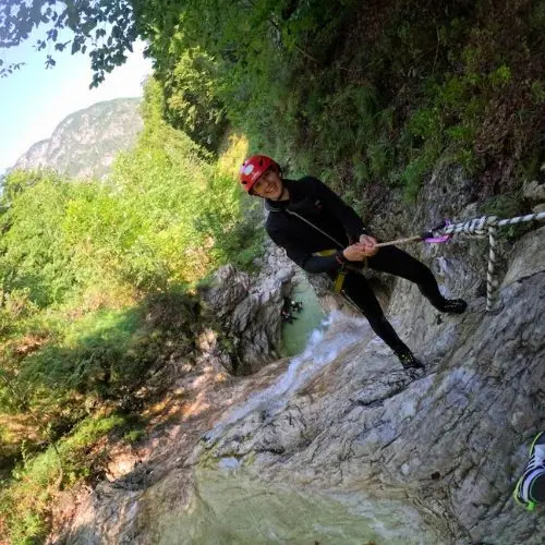 A happy female guest smiling at the camera while sliding down a smaller waterfall in Fratarica canyon.