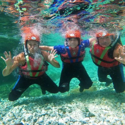 An underwater GoPro shot of a mother, father, and son swimming in the emerald Soča River during a rafting trip.