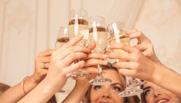 A close-up photo of a group of bridesmaids toasting with champagne glasses during a bachelorette party wine tasting trip.