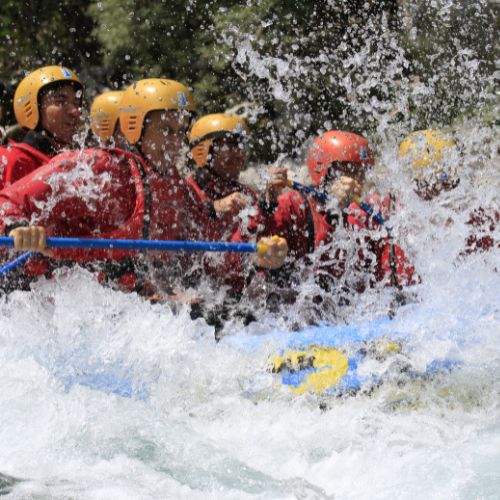 Amici con caschi gialli e rossi immersi negli schizzi d'acqua durante una sessione di rafting per addio al celibato a Bovec, sull'Isonzo.