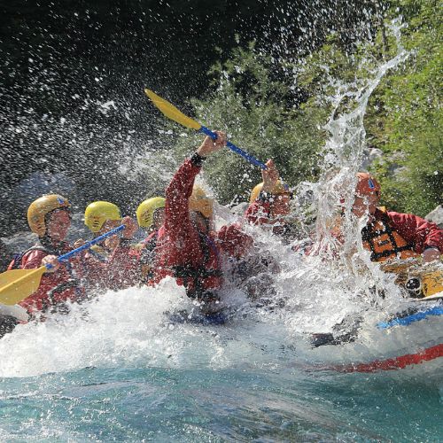 Un gruppo di amici festeggia un addio al celibato facendo rafting a Bovec, Slovenia, su un gommone blu tra gli schizzi.