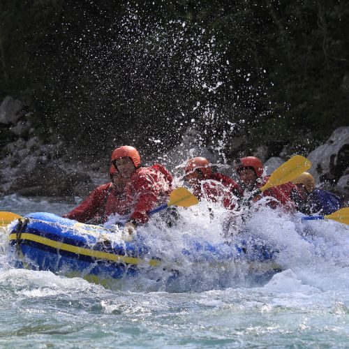 Vista posteriore di un gruppo di ragazzi con caschi rossi che fanno rafting sull'Isonzo per un addio al celibato a Bovec, circondati dalla natura.