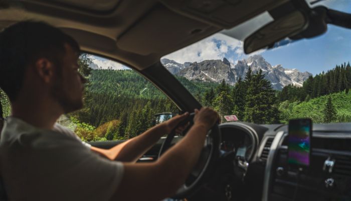 Scenic Drive to Bovec - Julian Alps Road Trip A man driving a car with a spectacular view of the majestic Julian Alps and green pine forests through the windshield on a road trip to Bovec, Slovenia.
